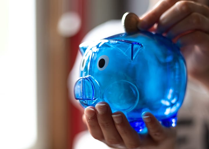 Hand stopt munt in een blauwe spaarpot, symbool voor stille financiële hulp.