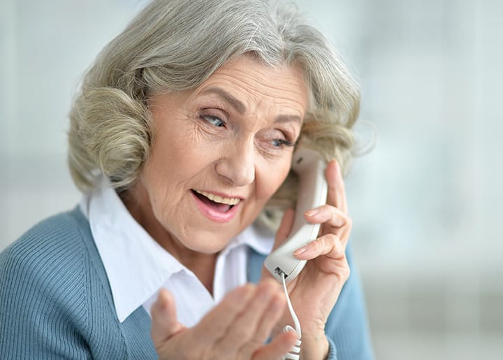 Oudere vrouw met grijs haar praat glimlachend aan de telefoon.